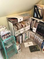 Photo of two shelves and the floor showing numerous sewing and embroidery books, patterns in folders and boxes, and assorted crafting supplies.