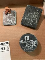 Lot view including rectangular soapstone with Inuit figure, rectangular soapstone with beaver, and round soapstone with howling wolf. Small reddish animal figure on Inuit piece.