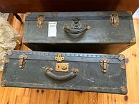 Top-down view of two black vintage suitcases side by side showing latch closures and leather handles