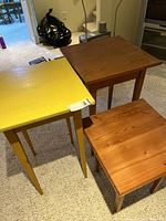 Three small wooden tables grouped together; two natural wood finish taller tables (18x18x30) and one shorter yellow table (18x18x21)