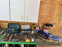 Wide shot of the workbench with various hand tools, caulking supplies, paint brushes, rivet setting tools, and adhesive tubes.