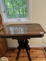 Full view of the antique Victorian style table showing the dark stained rectangular tabletop with beveled edges under natural light by a window.