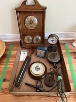 Full view of lot contents showing vintage barometer in wooden case and various small clocks, thermometers, and mechanical items on floor