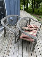 Two grayish-brown outdoor wicker sofas on wooden deck with striped cushions on one sofa, visible damage on one sofa.