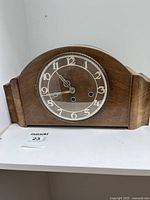 Front view of wooden mantel clock showing clock face with numbers, glass cover, and winding keyholes.