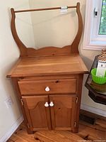 Full front view of wooden washstand with natural wood finish featuring drawer, doors, and towel bar.