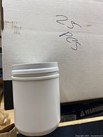 Close-up view of a single white plastic container with attached lid to show material and screw-top design, set against a cardboard box labeled '25 pcs'.