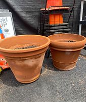 Two terra-cotta planter pots shown side by side on pavement. Both are filled with soil and show some dirt marks on exterior.