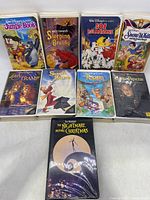 Nine children's VHS movies arranged on a surface including Disney classics and one Tim Burton movie