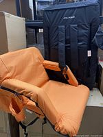Front view of one Alpcour stadium seat showing orange padded seat and black backpack frame with side pockets