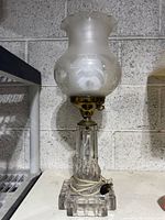Full view of antique hurricane lamp showing frosted etched glass shade and clear glass ridged base with brass fittings.