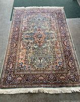 Full view of the rectangular oriental style area rug carpet with fringed edges and patterned borders on a concrete floor.