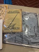 Close-up photo showing several cookbooks including 'Aunt Sammy's Radio Recipes Revised' and a 1963 West Virginia Centennial Cooking book in protective sleeves.