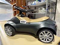 Side view of green and tan ride-on toddler toy car resembling a BMW, showing seat and wheels