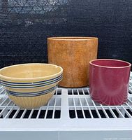 Front view of three ceramic items on white wire rack: large brown planter, cream bowl with blue stripes, and maroon planter.