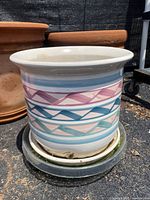 Ceramic flower pot showing colorful geometric pattern bands in pink, blue, and teal on white background, sitting on a plastic wheeled base.