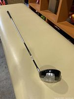 Full view of the golf driver showing the metallic shaft and clubhead, lying on a beige surface.