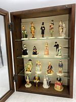 Full view of wooden case with 17 ceramic miniature figurines arranged on three glass shelves.