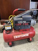 Side view of red Craftsman air compressor showing 125 PSI, 1.5HP, 3 GAL markings on black motor housing and brand on tank.