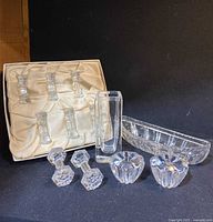 Photo showing the entire lot arranged on a black background: six cut crystal dumbbells in satin-lined box, rectangular vase, canoe boat-shaped relish dish, and a pair of flower-shaped small candle holders.