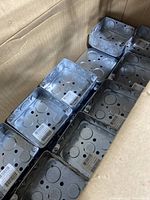 Photo showing multiple double metal electrical gang boxes stacked in a cardboard box, visibly new with barcodes.