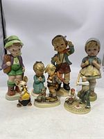 Full front view of nine ceramic figurines, mainly children in traditional costumes and animals arranged standing close together on a flat surface.