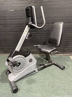 Side view of the Gold's Gym recumbent exercise bike showing padded seat, handlebars, and flywheel housing.