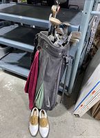 Nike black golf bag with hanging towels, filled with various golf clubs, and a pair of white and brown Etonic golf shoes size 8 on the floor beside it.