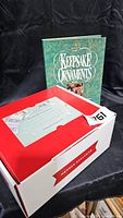 Photo showing green hardcover book titled 'Keepsake Ornaments' standing behind a large white and red box with a holiday-themed label on top.