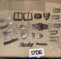 Full view of assorted Harley Davidson belt buckles, belt ends, and logo nameplates arranged on surface.
