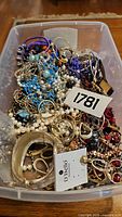 Overhead view of bin filled with assorted costume jewelry including bracelets, earrings, and necklaces in various colors and materials.