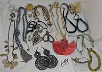 A top view of multiple assorted costume jewelry pieces including necklaces, earrings, bracelets, rings, and pendants arranged on a white surface.