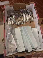 Box with approximately 40 pieces of Lenox flatware including forks, knives, and spoons, along with several unopened Lenox flatware set boxes.