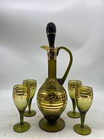 Full view of decanter with stopper and 5 matching glasses arranged around it, showing olive green glass with gold banding.