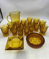 View of the full mid century amber glassware set including pitcher, glasses and ashtrays from front angle