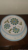 Stacked set of 6 dinner plates and one charger/platter showing floral design and blue trim