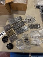 Overview of various metal belt buckles and parts including rectangular buckles, black rose-shaped buckles, Harley Davidson logo nameplates and other hardware