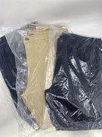 Three pairs of men's chino pants packed in clear plastic bags, navy and khaki colors visible