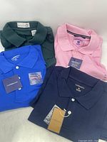 Four men's XL short sleeve collared polo shirts in solid colors shown folded together: dark green, pink, bright blue, and navy blue.