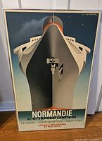 Full view of framed Normandie shipping line art poster, showing bow of the ship with title and route information.