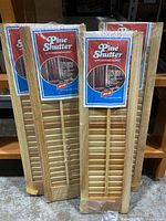 Four new old stock pine shutters with moveable louvers packaged in original plastic wrap, shown leaning against shelf.