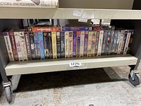 Shelf view showing 35 VHS movies in original shrink wrap, assorted titles and movie genres