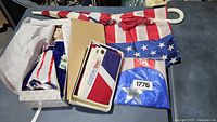 Overview of entire lot showing large American flag on pole, patriotic doll in box, folded flag, umbrella, and blue '1776' cloth.