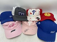 Front view of six hats arranged with Phillies logos visible and one Eagles hat