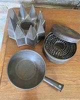 Photo showing the grouping of three primitive tin molds: a large star-shaped mold, nesting small round molds inside a container with lid, and a perforated handled tin mold.