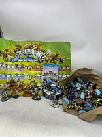 Wide shot showing Skylanders figurines, portal, the promotional poster, and game disc/case placed together on a white background.