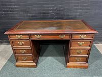 Front view of the vintage Sligh Partners desk showing the leather top with gold tooling and brass hardware on the drawers.