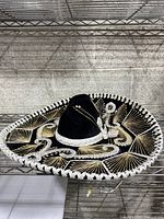 Black mariachi sombrero hat on metal shelf, showing decorative silver and white embroidery and silver edge trim.