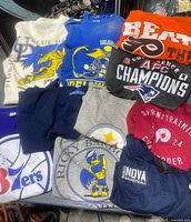 Lot of 9 vintage sports t-shirts and one navy Nike basketball polo shirt stacked on a surface, showing various team names and logos.