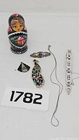 Overview of entire lot showing the nesting doll, bracelet, peacock pendant, triangular pendant, and bar brooch
